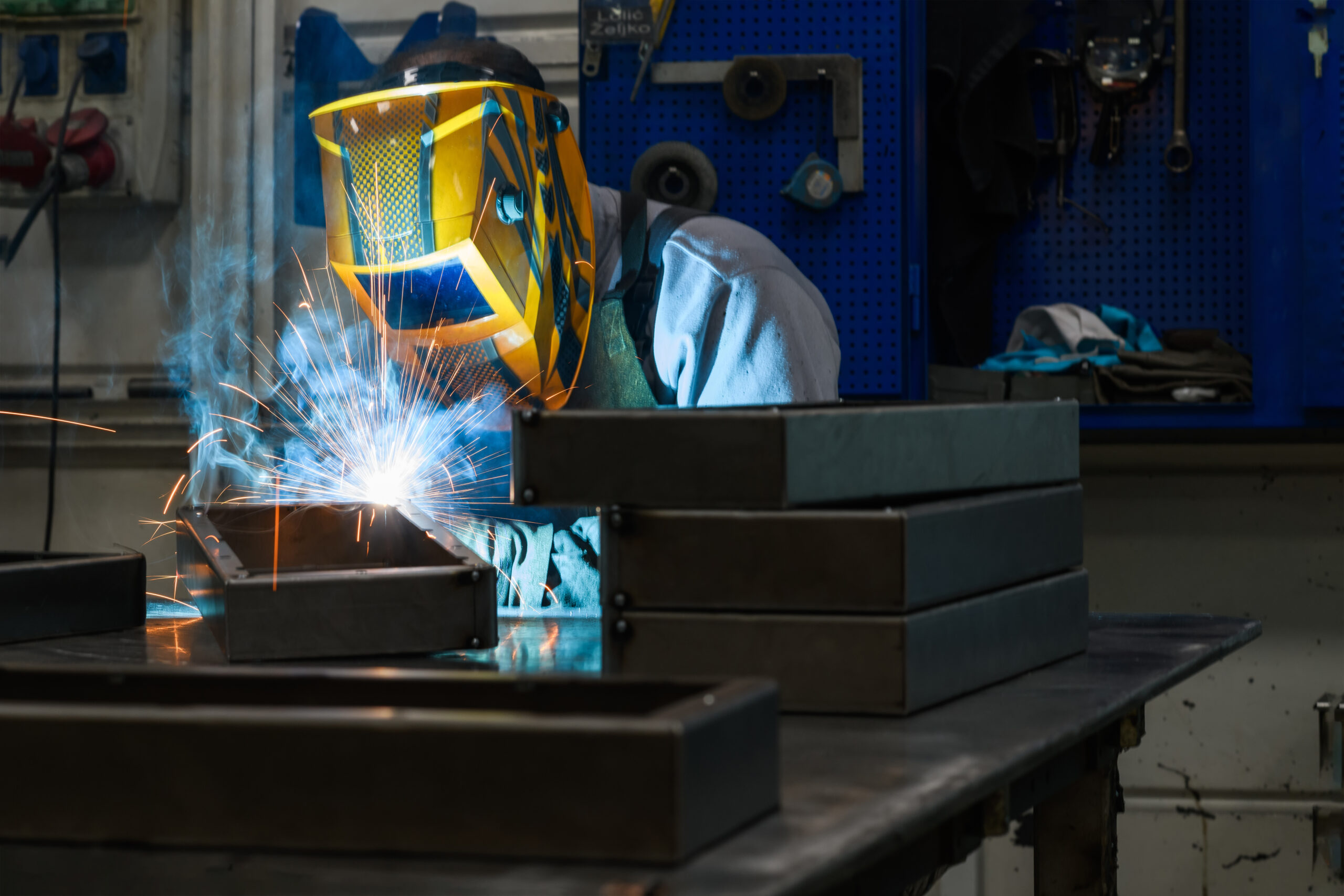 Welding with a full face shield and sparks at a metal workbench